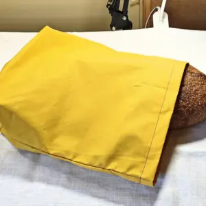 Yellow waxed cotton bread bag with a loaf tucked inside, resting on a light cloth